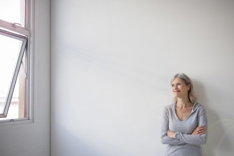 Smiling Caucasian woman leaning on wall near window