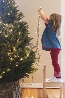 Caucasian girl hanging lights on Christmas tree