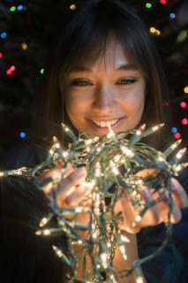 Mixed Race woman holding string lights near Christmas tree