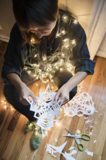 Mixed Race woman sitting on floor wrapped in string lights holding snowflake