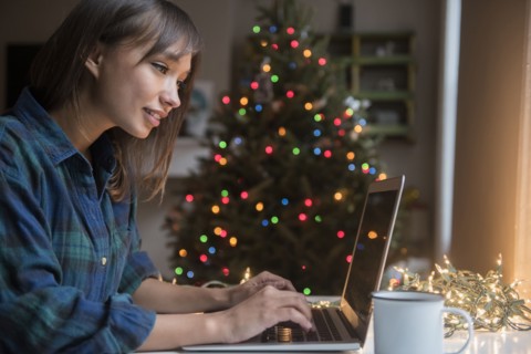 Mixed Race woman using laptop near Christmas tree