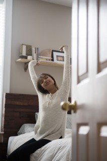 Mixed Race woman stretching arms on bed