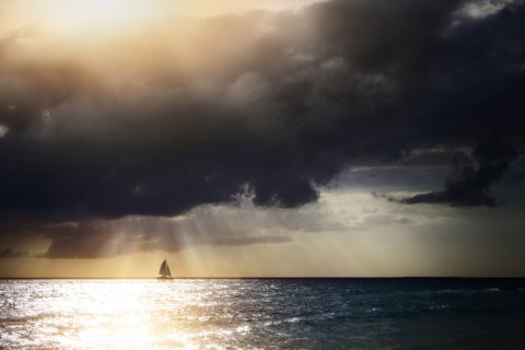 Sunbeams through storm clouds over sailboat