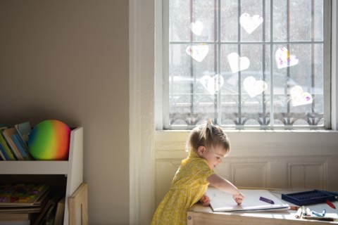 Caucasian baby girl coloring on sketchpad near window