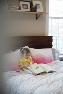 Caucasian baby girl sitting on bed reading book