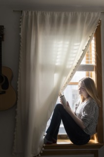 Smiling woman sitting in window using digital tablet