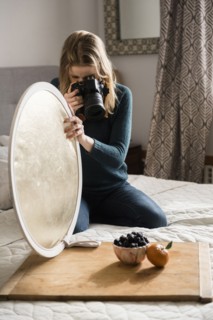 Woman kneeling on bed holding reflector photographing fruit