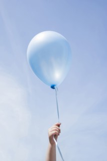 Hand of Caucasian girl holding blue balloon in blue sky