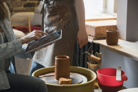 Caucasian women using digital tablet near pottery wheel