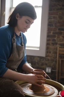 Caucasian woman shaping clay on pottery wheel