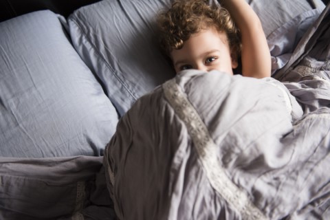 Caucasian boy hiding under blanket in bed