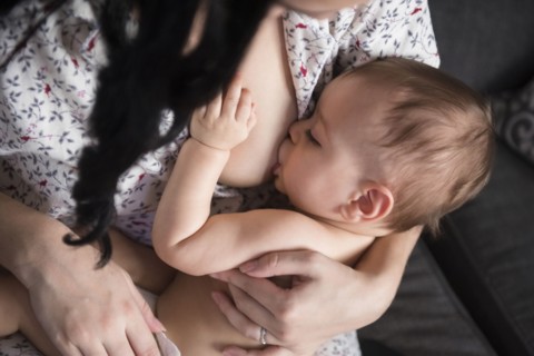 Caucasian mother breastfeeding baby son on sofa