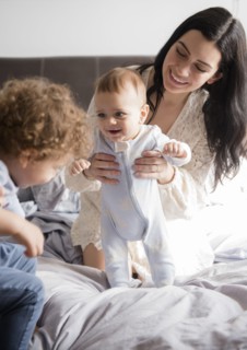 Caucasian mother kneeling on bed playing with sons