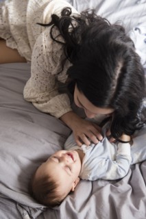 Caucasian mother laying on bed tickling baby son