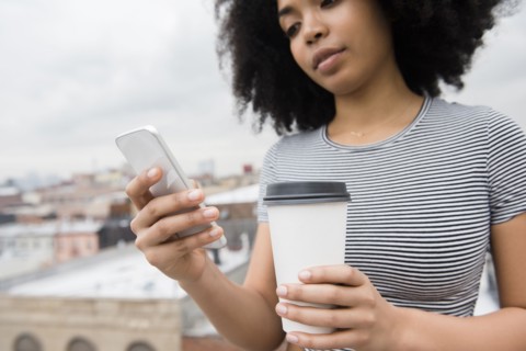 African American woman drinking coffee and texting on cell phone