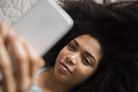 African American woman laying in bed texting on cell phone