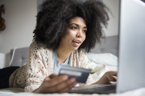 African American woman laying in bed online shopping with laptop