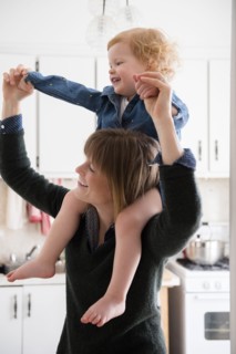 Caucasian mother carrying daughter on shoulders in kitchen