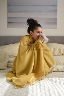 Hispanic woman sitting on bed wrapped in blanket drinking coffee