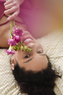 Hispanic woman laying on bed holding flowers
