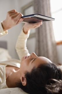 Hispanic woman laying on bed reading digital tablet