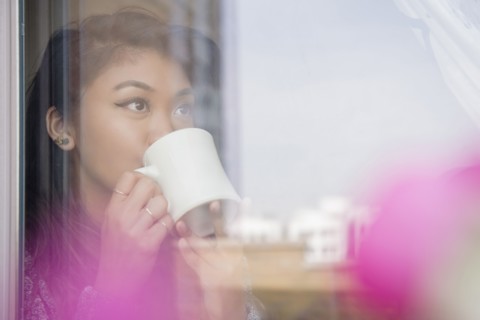 Mixed Race woman drinking coffee behind window