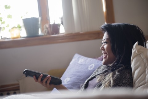 Smiling Mixed Race woman holding remote control and watching television