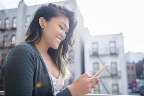 Mixed Race woman texting on cell phone in city
