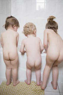Naked Caucasian boy and girls standing near bathtub