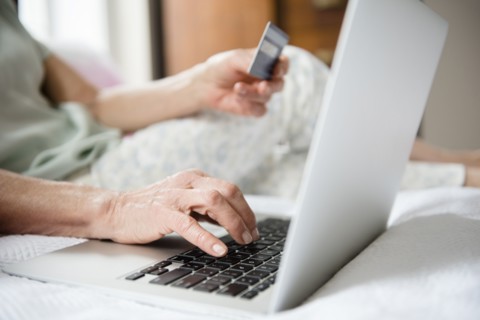 Hands of older woman shopping online with credit card and laptop
