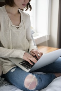 Caucasian woman sitting on bed using a laptop