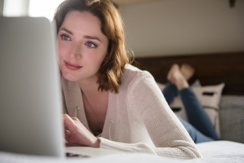 Caucasian woman laying on bed using a laptop