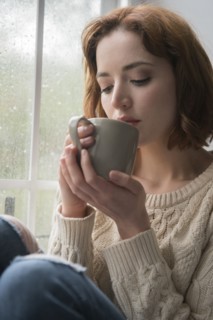 Caucasian woman drinking coffee near rainy window