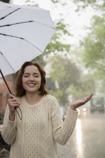 Carefree Caucasian woman holding umbrella in rain