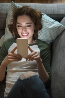 Caucasian woman laying on sofa texting on cell phone