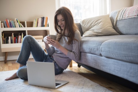 Caucasian woman sitting on floor with coffee and laptop