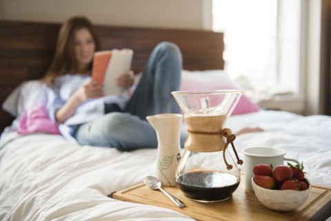 Caucasian woman laying in bed reading book near breakfast tray