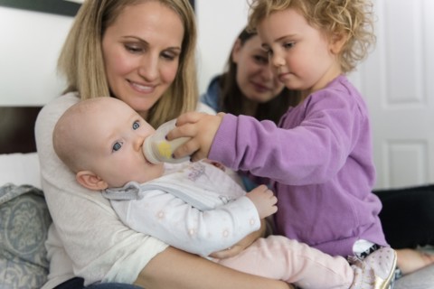 Caucasian girl feeding bottle to baby sister