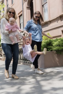 Caucasian mothers swinging daughter on city sidewalk