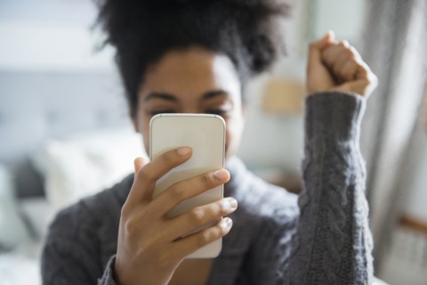African American woman celebrating while texting on cell phone