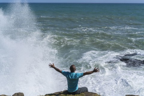Chinese man sitting on cliff at ocean