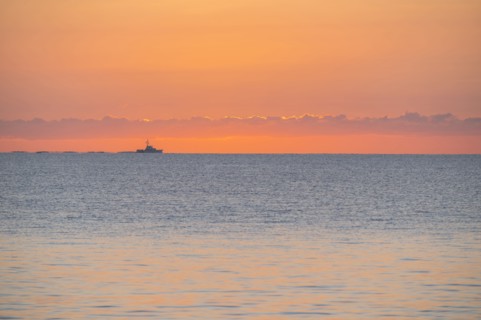 Calm sea at sunrise with fishing boat in distance