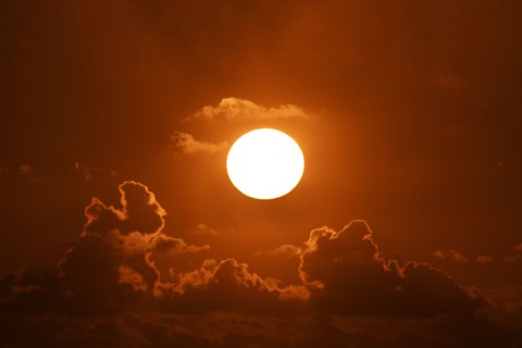 Bright sun at sunset with clouds against orange sky