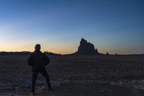 Silhouette of man looking at Ship Rock at sunset
