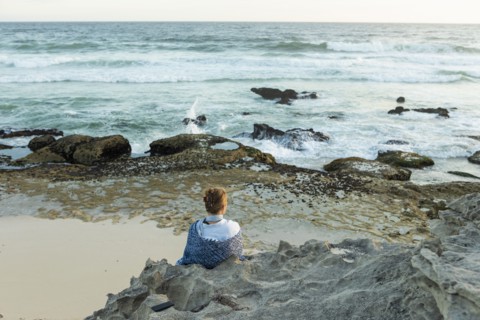 Girl sitting on beach looking at ocean