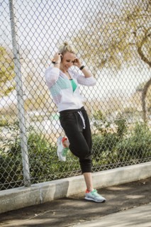 Smiling athlete woman with headphones leaning against fence