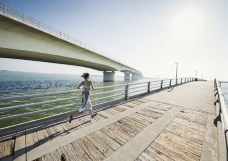 Rear view of woman jogging on bridge on sunny day