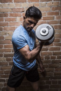 Man exercising with dumbbell against brick wall