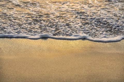 Close-up of ocean wave on sand at sunset