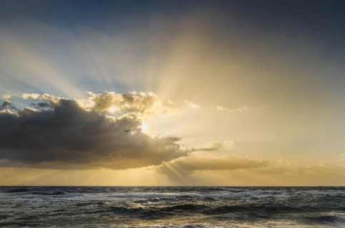Sun rays bursting from behind clouds above sea at sunrise